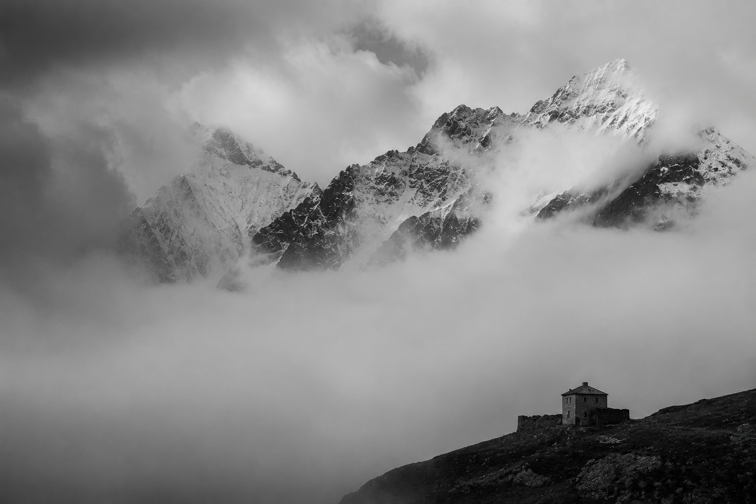 A single house beneath snow-bound peaks emerging from cloud